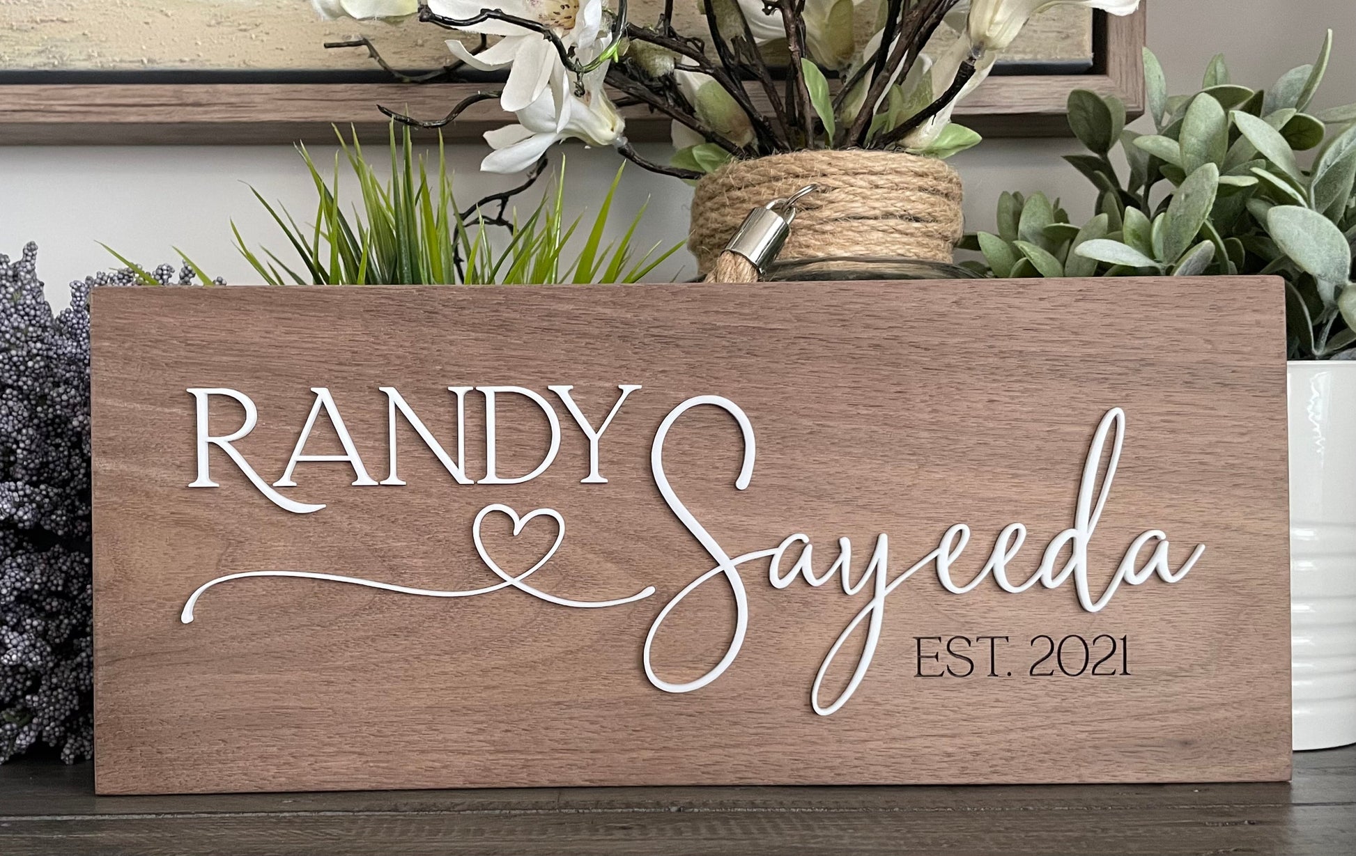 Wooden sign with 'RANDY Sayeeda EST. 2021' text, surrounded by plants.