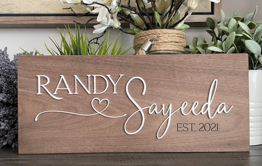 Wooden sign with 'RANDY Sayeeda EST. 2021' text, surrounded by plants.